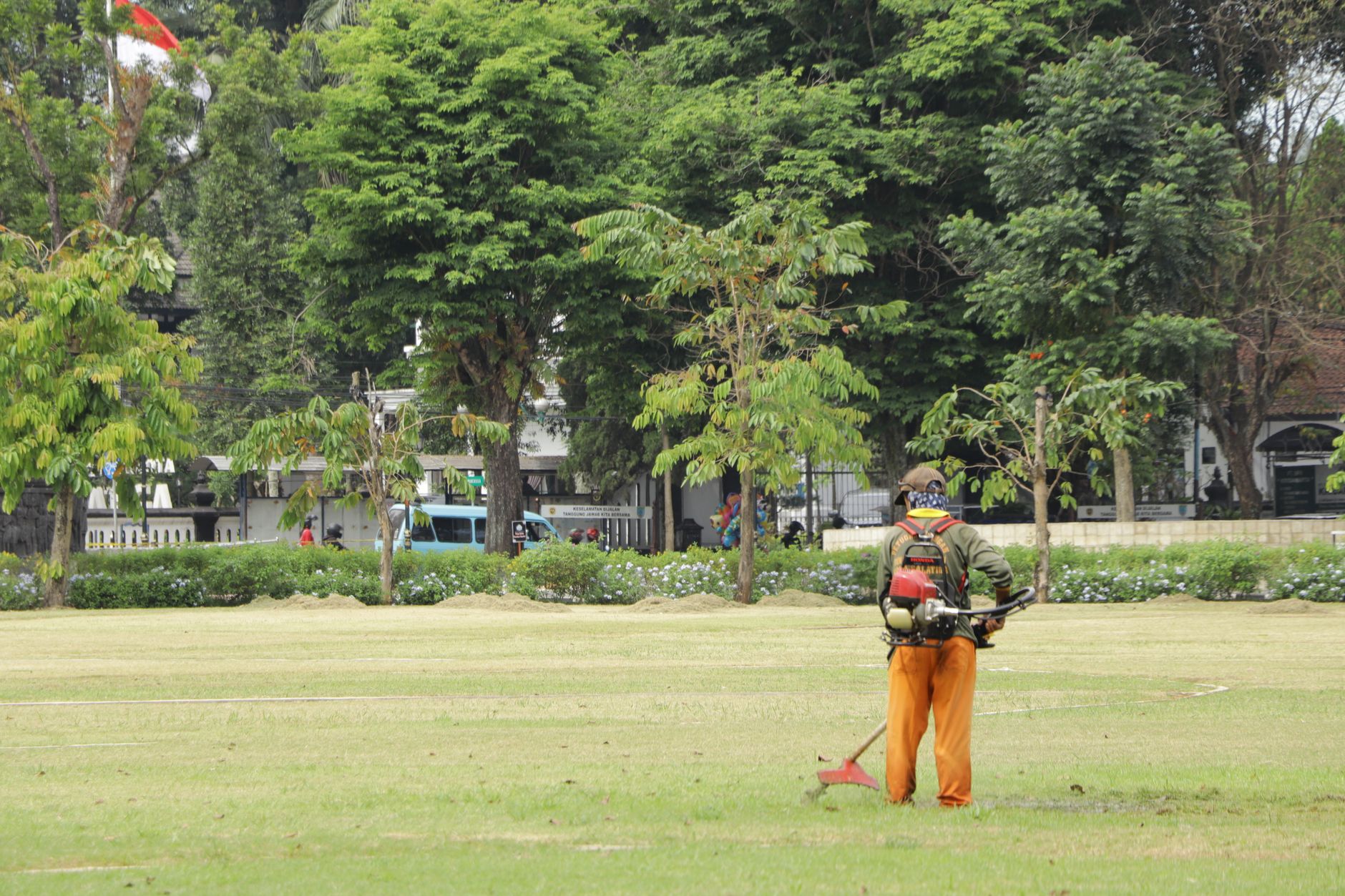 A worker cutting grass with a lawn mower, with trees in the background.