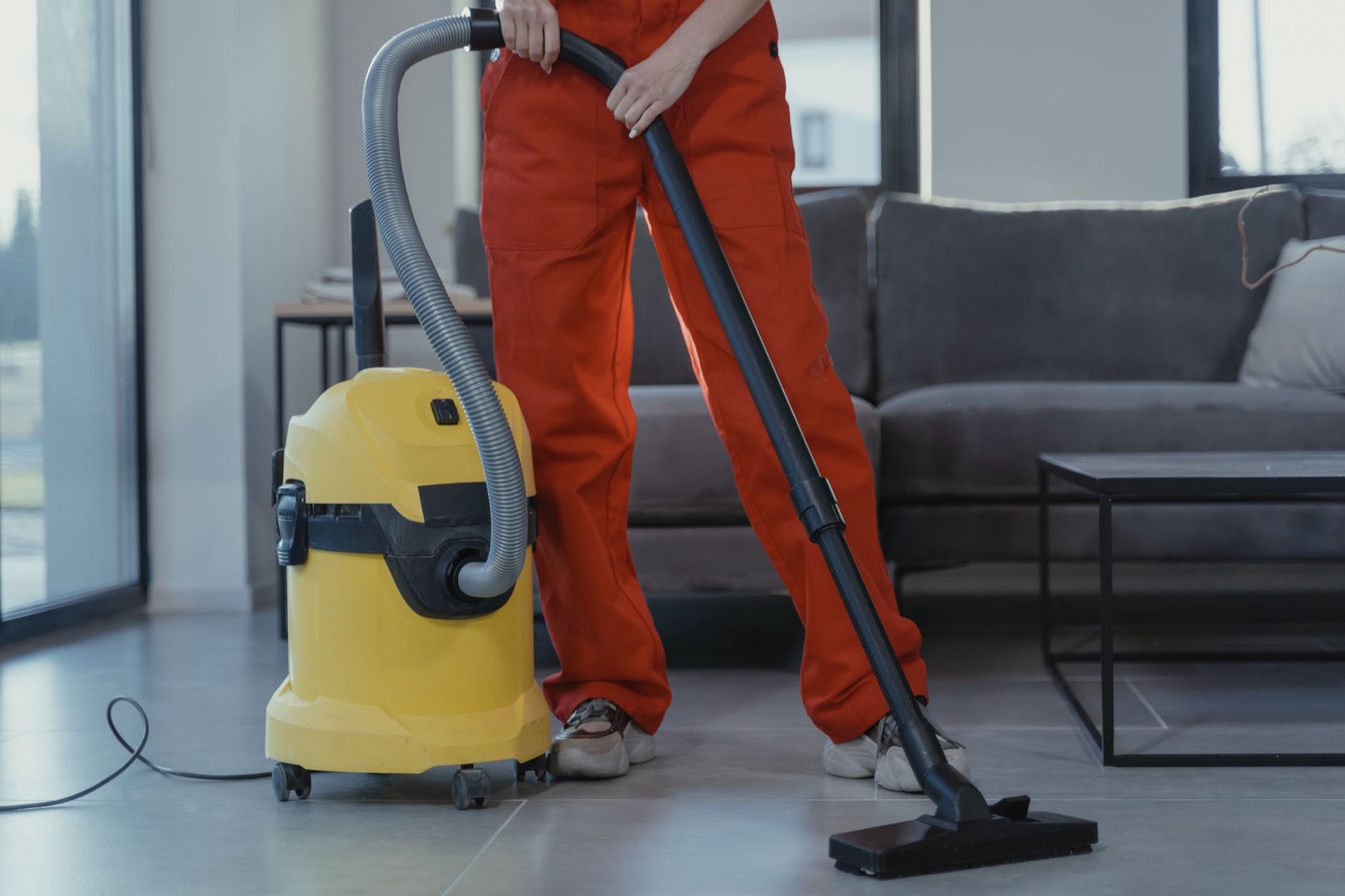 A professional cleaner in coveralls running a vacuum over living room carpet