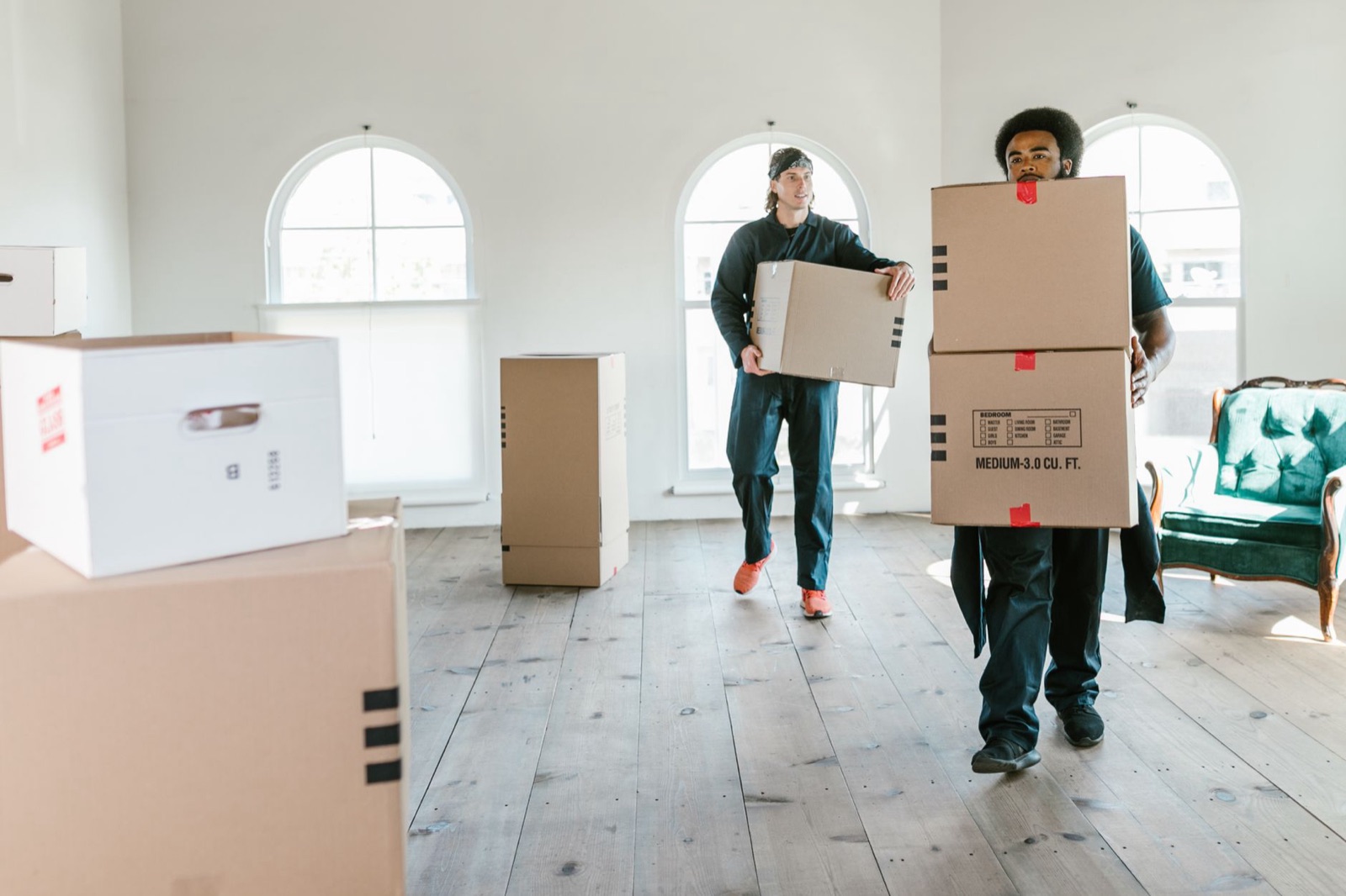 Two uniformed movers carrying stacked cardboard boxes through a bright room